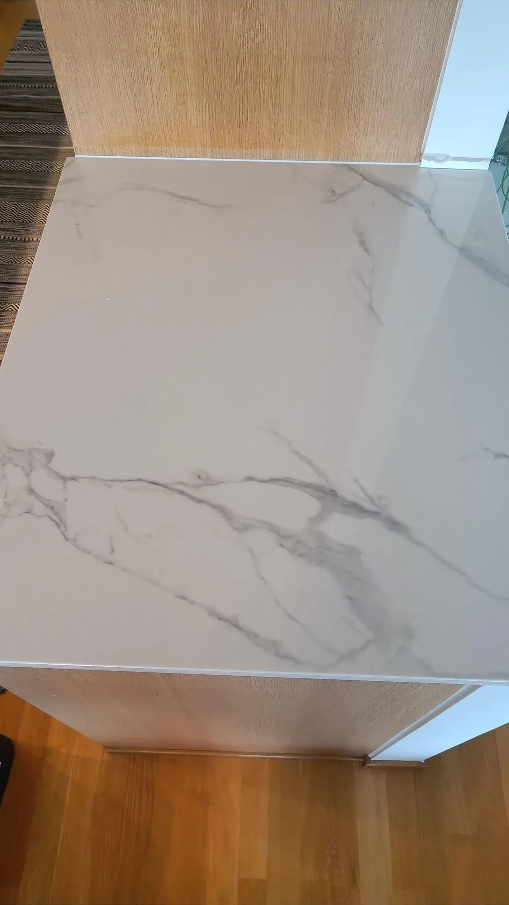 Ovanvy av polerad Dekton Natura bänkskiva med vit marmoreffekt och träinredning i ett kök i Limhamn.