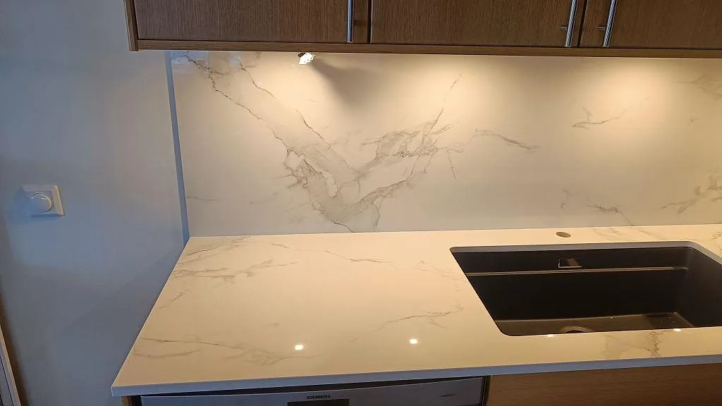 Polerad köksbänkskiva i Dekton Natura med underlimmad diskho och marmorerat stänkskydd under överskåp i Limhamn.