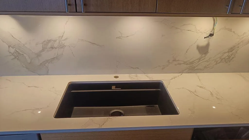 Underlimmad diskho i polerad Dekton Natura, vit keramik med grå ådring och matchande stänkskydd i Limhamn.