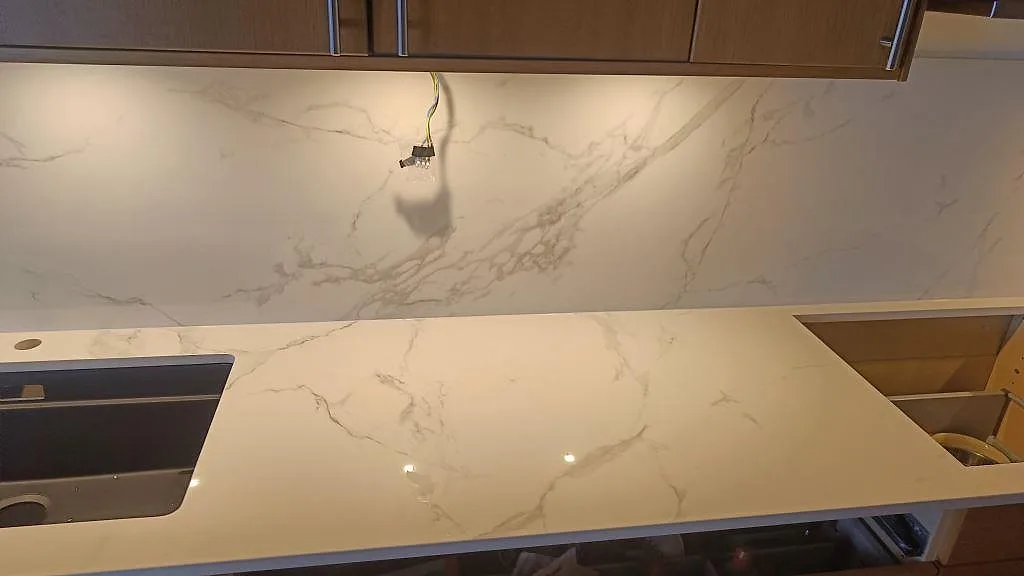 Bänkskiva i polerad Dekton Natura med hällurtag, underlimmad diskho och hög stänkvägg i ett kök i Limhamn.