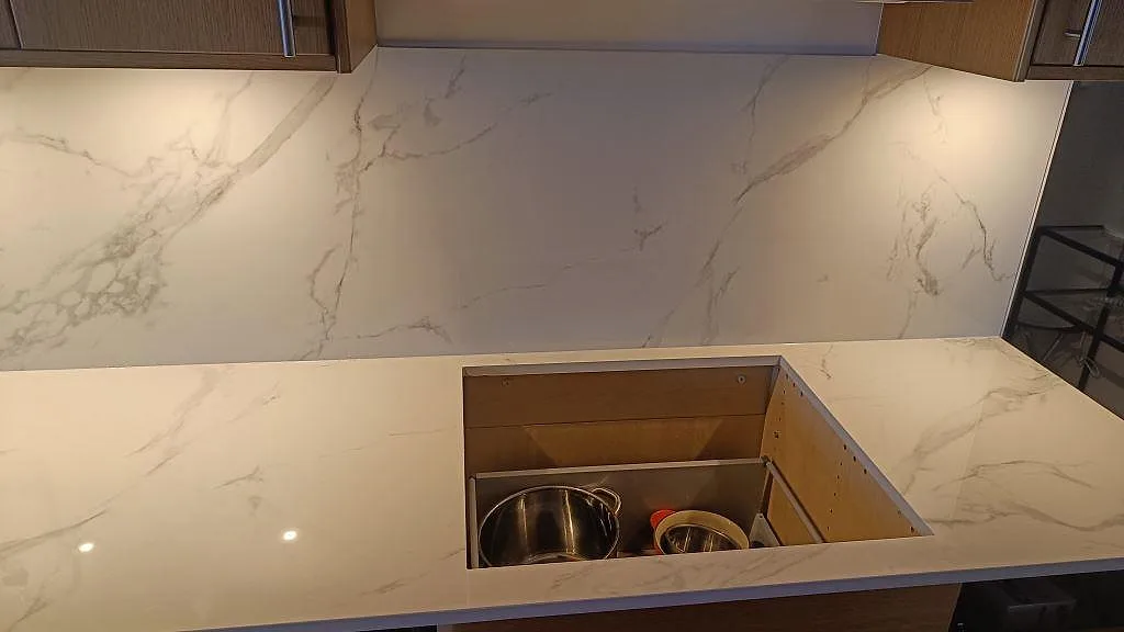 Hällurtag i polerad Dekton Natura med vit marmorerad keramik och stänkskydd vid varm träinredning i Limhamn.