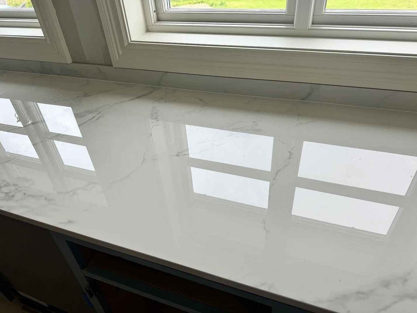 Närbild på polerad Dekton Natura köksbänkskiva i keramik där fönstren speglas i den ljusa ytan i Tjureda.