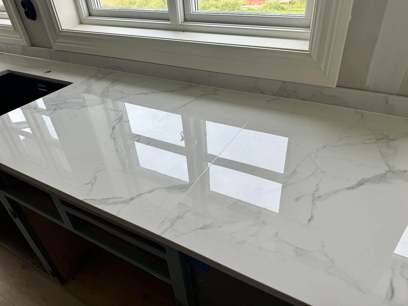 Polerad Dekton Natura bänkskiva med marmorlik ådring, svart diskho och matchande stänkskydd i ett kök i Tjureda.