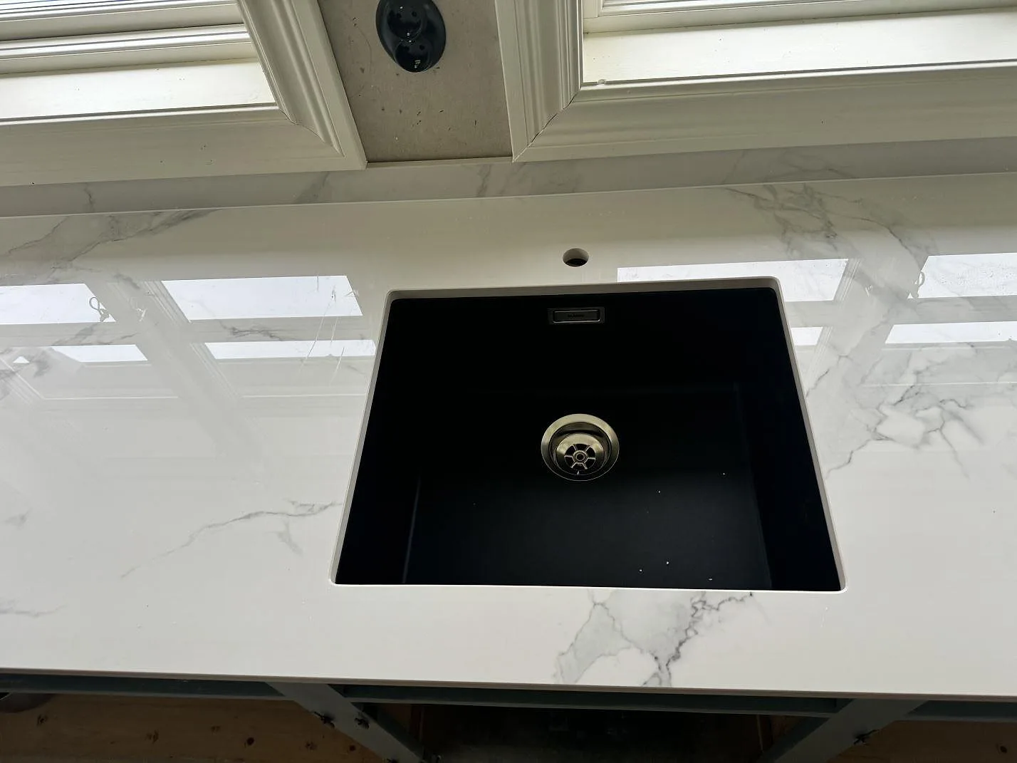Svart diskho i en polerad Dekton Natura köksbänkskiva med låg stänkkant under fönster i Tjureda.
