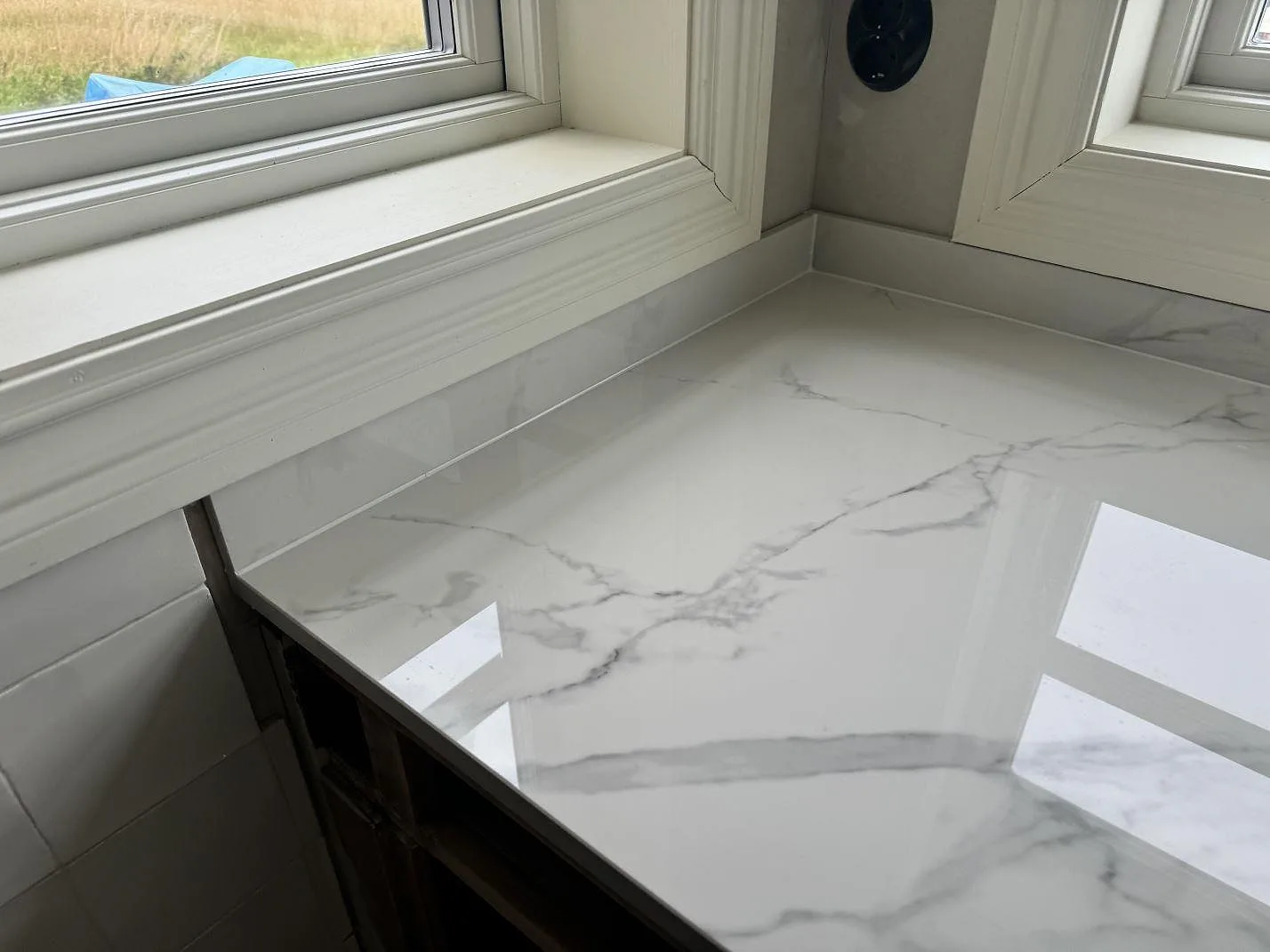 Detalj av polerad Dekton Natura bänkskiva i hörn med låg stänkkant och grå ådring i ett kök i Tjureda.