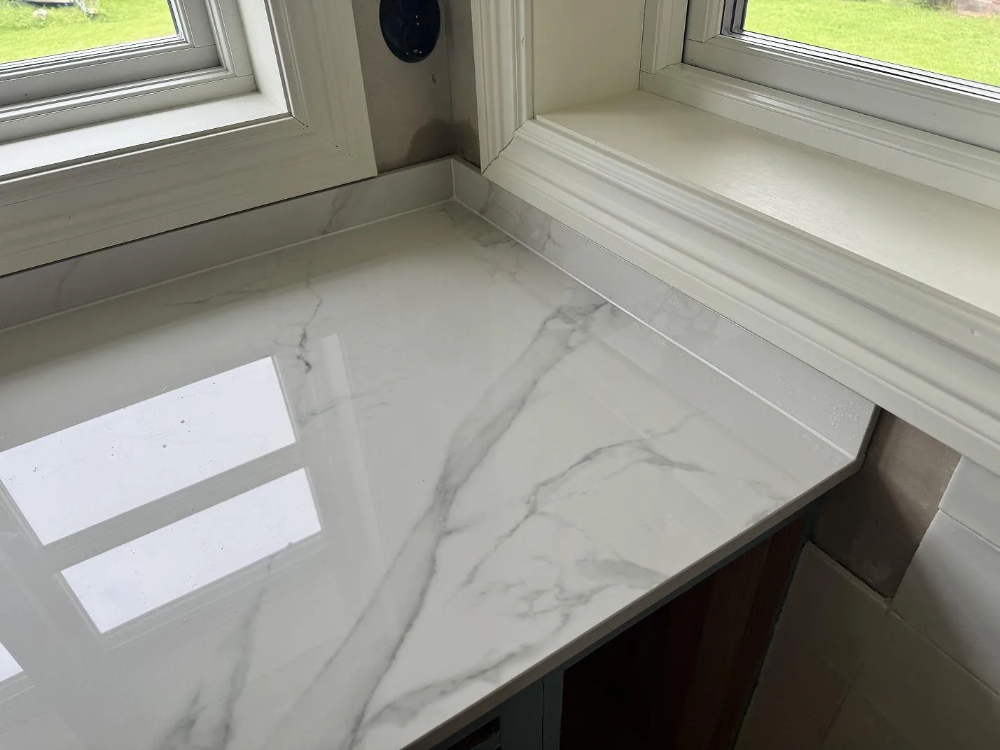 Hörnparti med polerad Dekton Natura köksbänkskiva och matchande stänkskydd intill fönster i Tjureda.