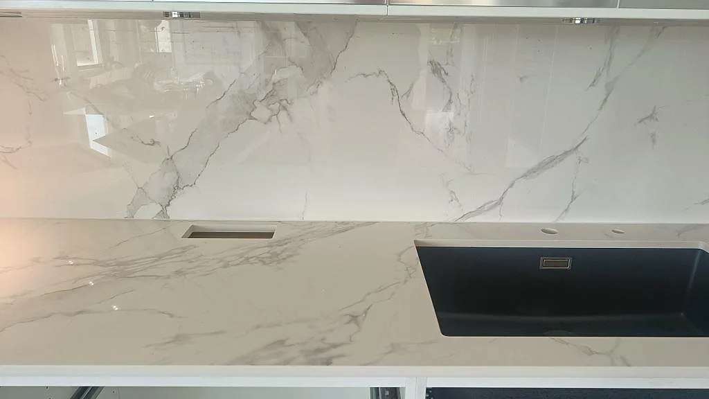 Polerad Dekton Natura köksbänkskiva med svart underlimmad diskho och uppvikt stänkskydd i samma keramik i ett kök i Växjö.