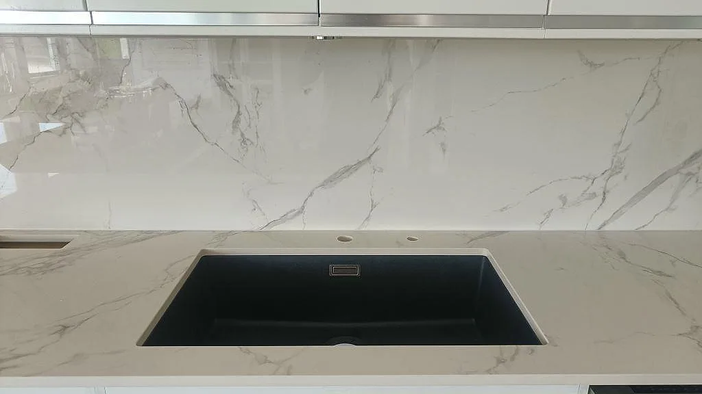 Närbild på svart underlimmad diskho i polerad Dekton Natura köksbänkskiva med fint grått marmormönster i ett kök i Växjö.