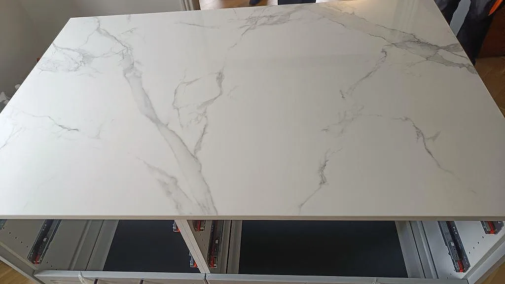 Köksö i polerad Dekton Natura med markant grå ådring och ljusinsläpp från fönster i ett kök i Vanløse.