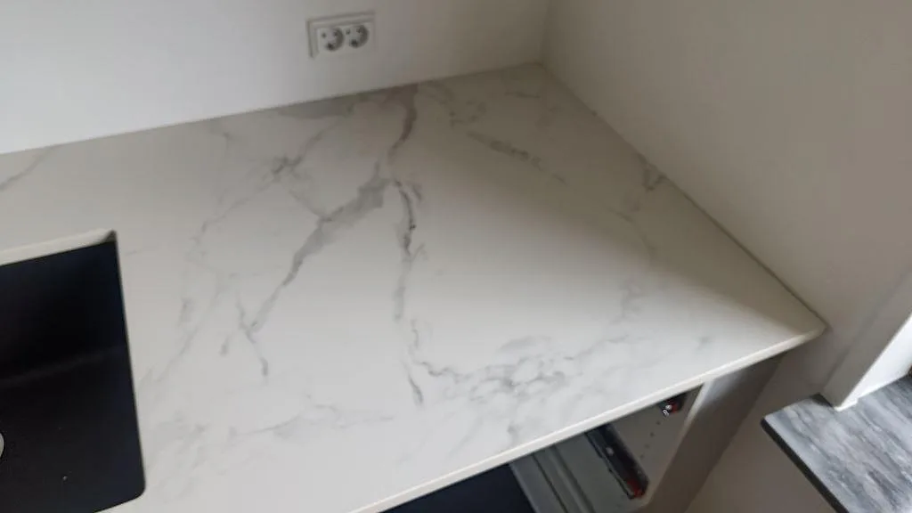 Köksö i Dekton Natura keramik med vit yta och grå ådring ovanför öppna lådstommar i ett kök i Vanløse.