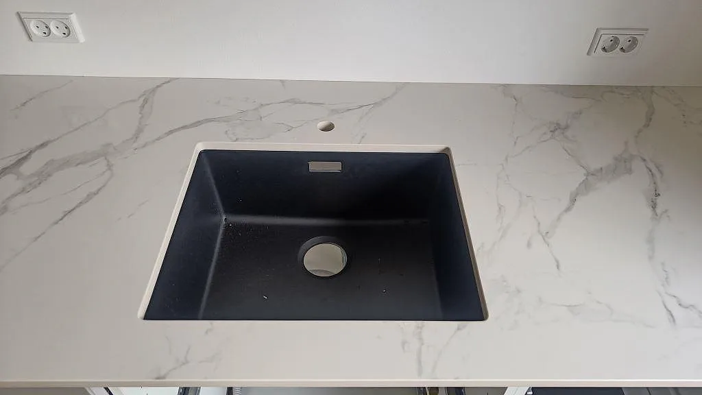 Underlimmad svart kompositdiskho i en köksbänkskiva av polerad Dekton Natura med grå ådring i ett kök i Vanløse.