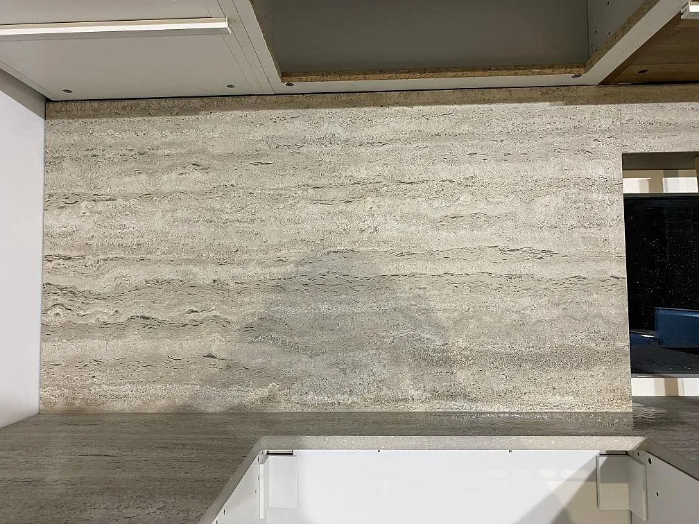 Stänkskydd och väggbeklädnad i matt Dekton Nebu keramik bakom en köksbänkskiva under montering i Borrby.
