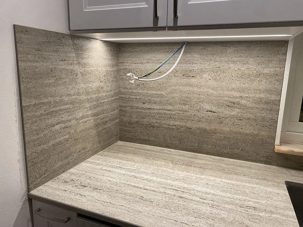 Hörndetalj av matt Dekton Nebu bänkskiva och uppvikt stänkskydd i keramik med belysning under överskåp i ett kök i Upplands Väsby.