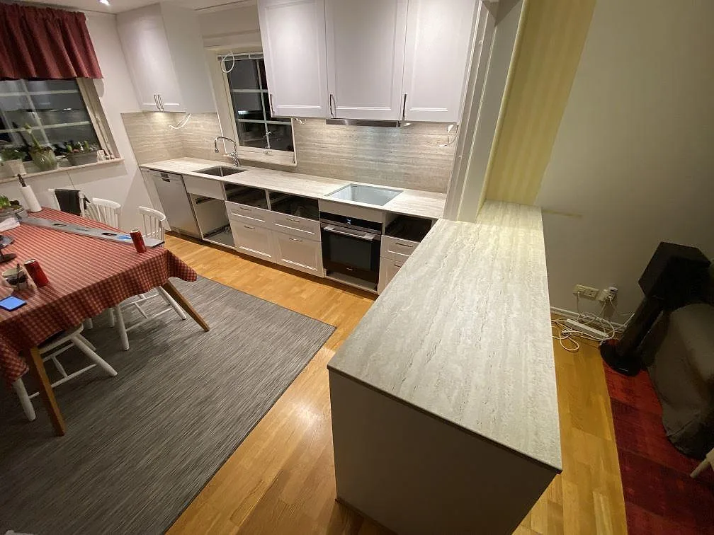 Översikt av kök i matt Dekton Nebu med L-formad bänkskiva och halvö i varmt gråbeige keramik, underlimmad diskho och uppvikt stänkskydd, Upplands Väsby.