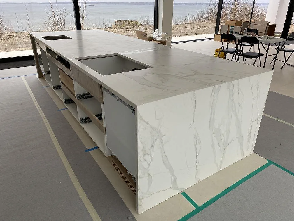 Lång köksö i matt Dekton Neural, ljus keramik med öppningar under montering i Ålsgårde.