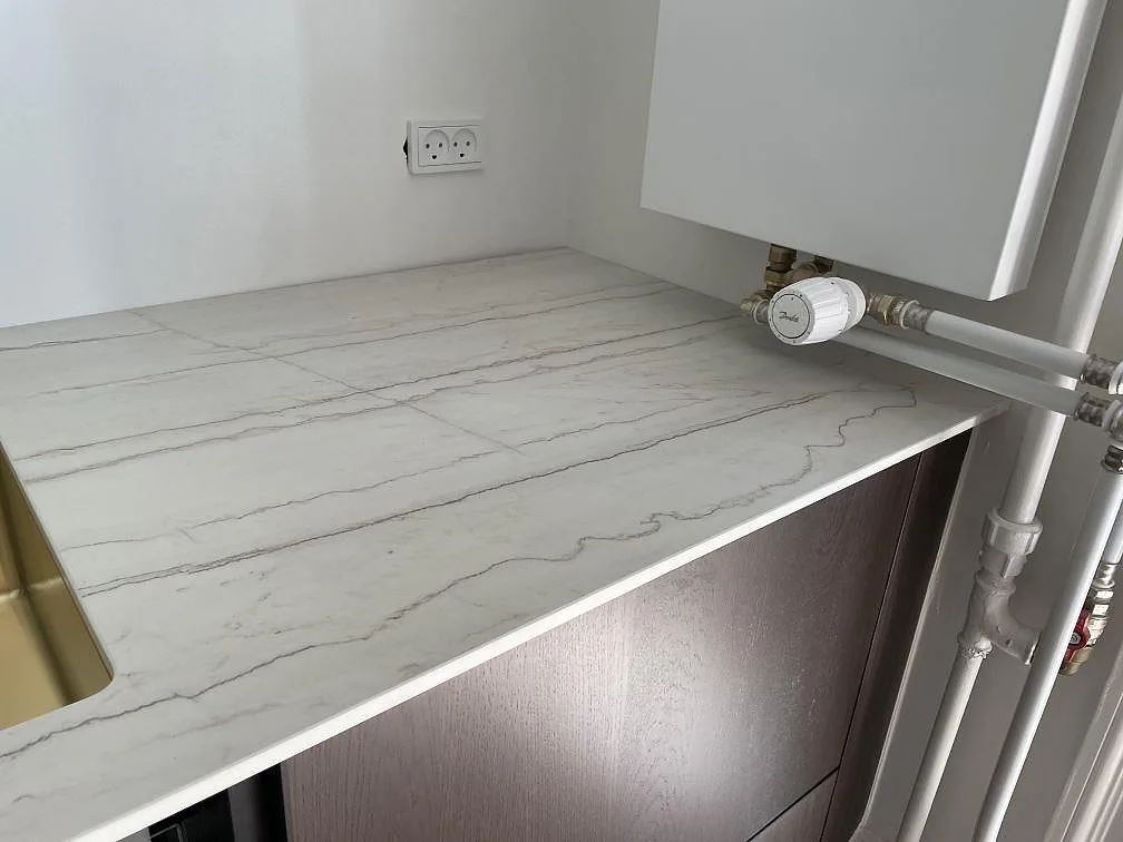 Retursida av köksbänkskiva i matt Dekton Neural med tunn framkant, vägguttag och synlig rördragning i Frederiksberg.