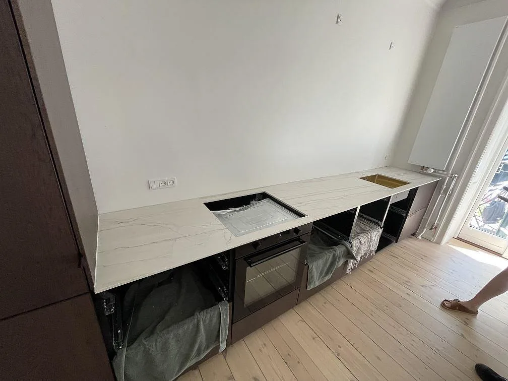 L-formad köksbänkskiva i matt Dekton Neural, 12 mm keramik, med guldtonad diskho och svart induktionshäll i Frederiksberg.