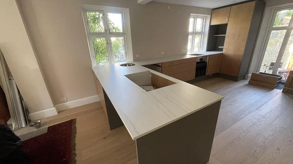 Köksbänkskiva i grå ådrad Dekton Neural keramik, matt, i en U-formad köksuppställning med köksö under montering i København V.