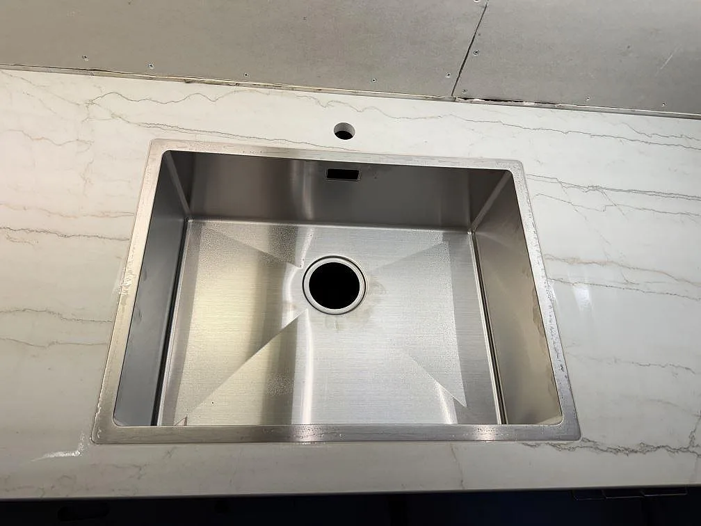 Detaljbild av rostfri diskho i en bänkskiva av matt Dekton Neural med ljus marmorerad ådring i Lund.