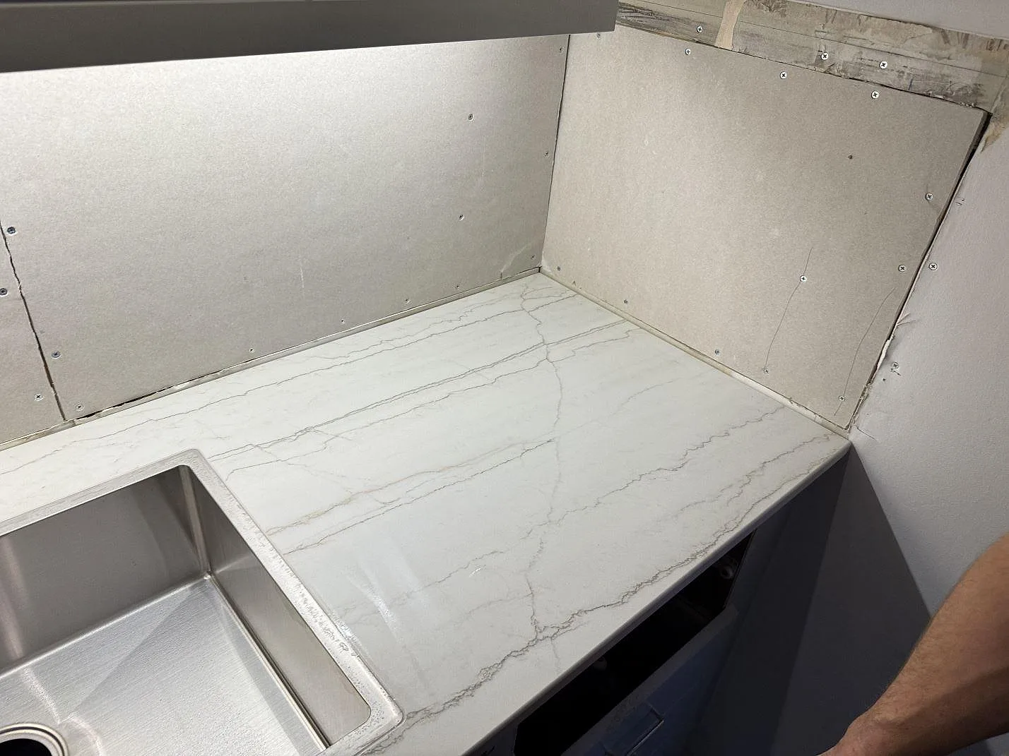Dekton Neural i matt keramik som köksbänkskiva med rostfri diskho, grå ådring och öppna väggytor under montering i Lund.