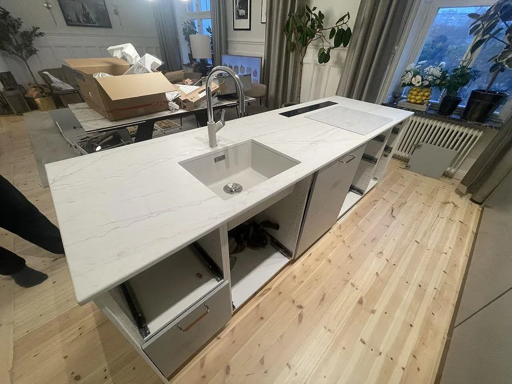 Matt köksbänkskiva i Dekton Neural, vit keramik med diskho, kran och synlig ådring under montering i Stockholm.