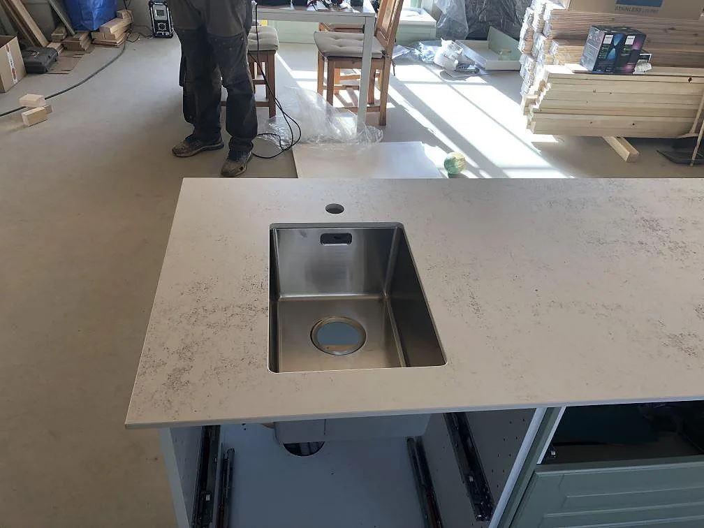 Köksö i Dekton Nilium, matt greige ultrakompakt yta, med underlimmad rostfri diskho i ett kök under montering i Båstad.
