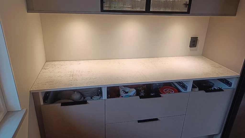 Rak köksbänkskiva i matt Dekton Nilium under väggskåp och belysning i Hörby.