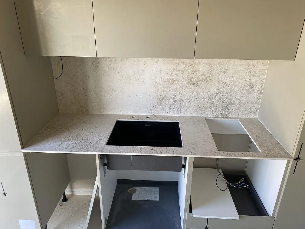 Köksbänkskiva i matt Dekton Nilium med full stänkvägg, svart ho och öppna skåpstommar i Tygelsjö.