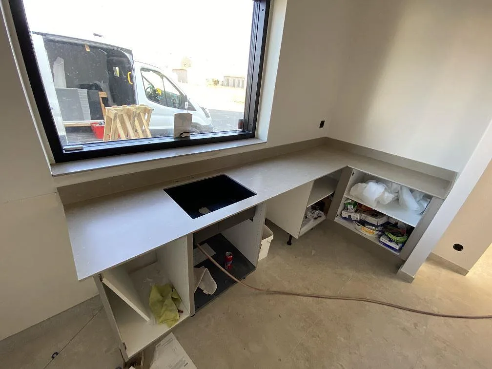 Ljust kök i Tygelsjö under montering med köksbänkskiva i matt Dekton Nilium, svart ho och arbetsyta under fönster.