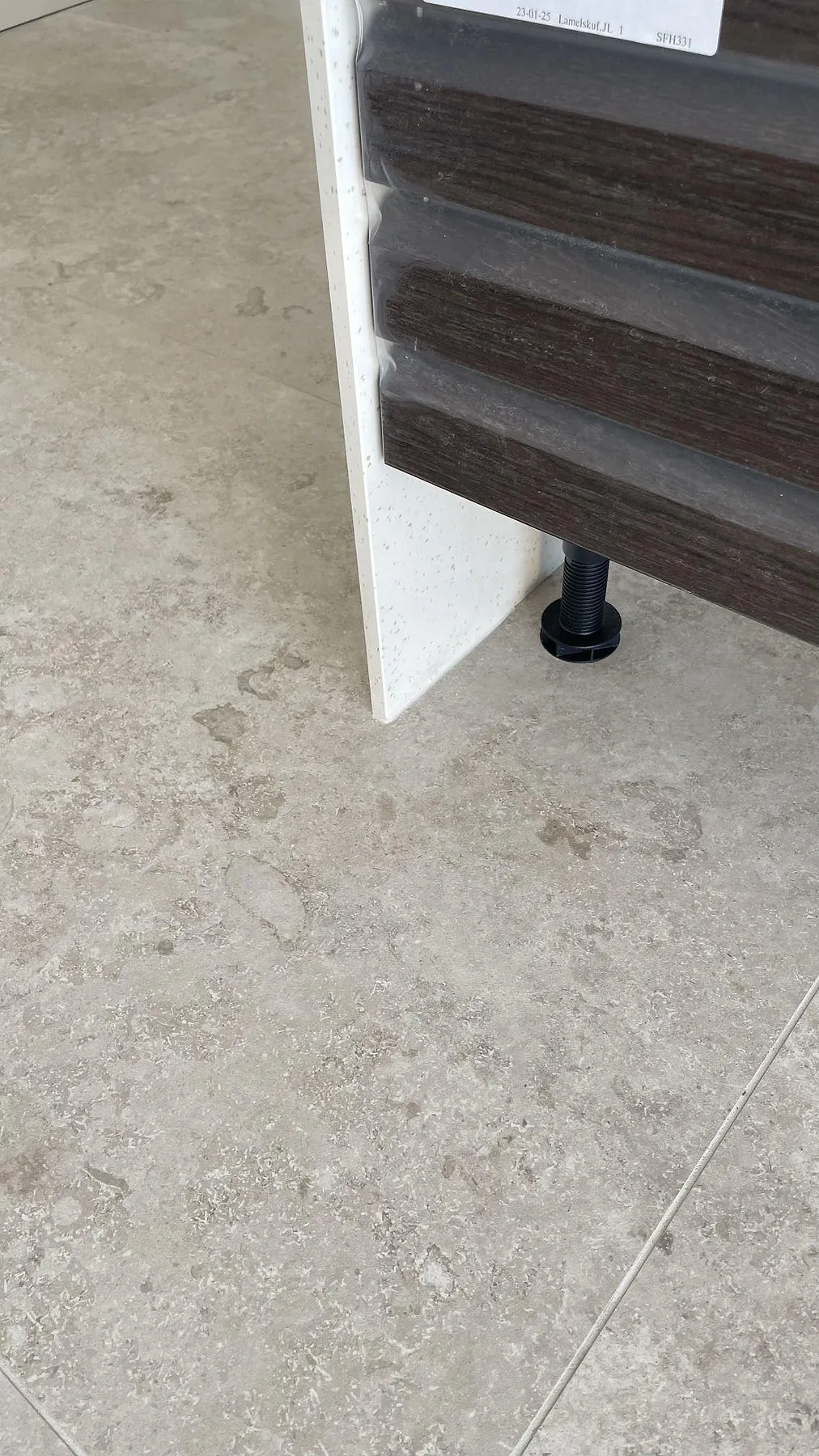 Närbild av matt Dekton Nilium som lodrätt sidostycke vid skåpstomme och grått golv under montering i Tygelsjö.