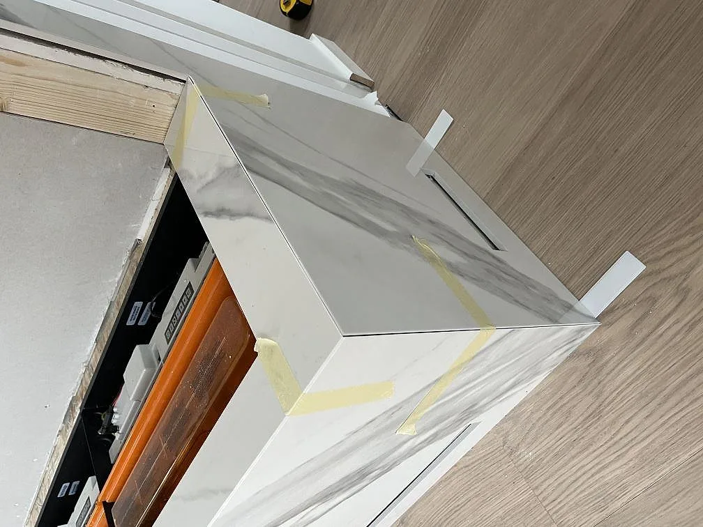 Hörn av Dekton Olimpo köksbänkskiva med uppvikt stänkkant vid fönster, polerad vit sten med grå ådring i Göteborg.