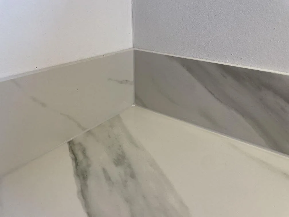 Närbild på 8 mm stänkkant och matt Dekton Opera Velvet bänkskiva i vit keramik med Calacatta-ådring i Solroed Strand.