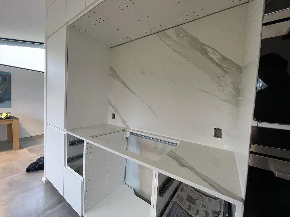 Köksbänkskiva och hög väggpanel i matt Dekton Opera Velvet keramik med hällöppning under montering i Solroed Strand.