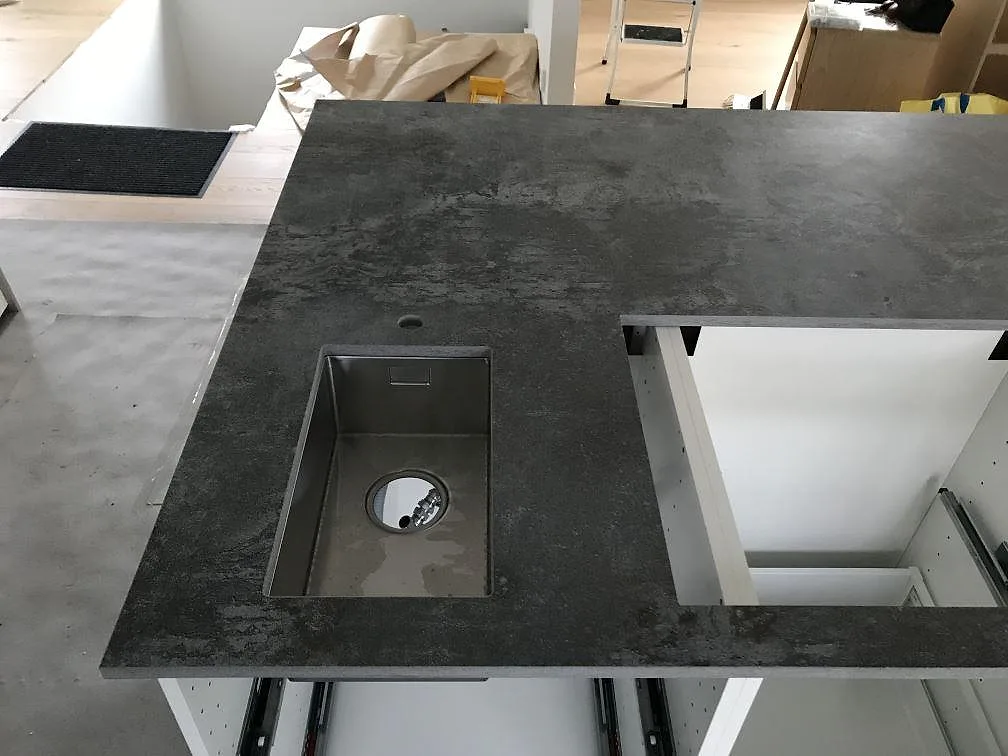 Köksbänkskiva och köksö i Dekton Orix, matt mörkgrå betongliknande keramik, med underlimmad rostfri diskho i ett kök i Sävedalen.
