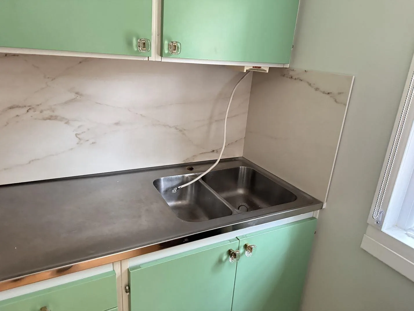 Sidopanel och stänkskydd i matt Dekton Rem (Velvet) vid den rostfria bänkdelen och fönstret i köket i Åhus.