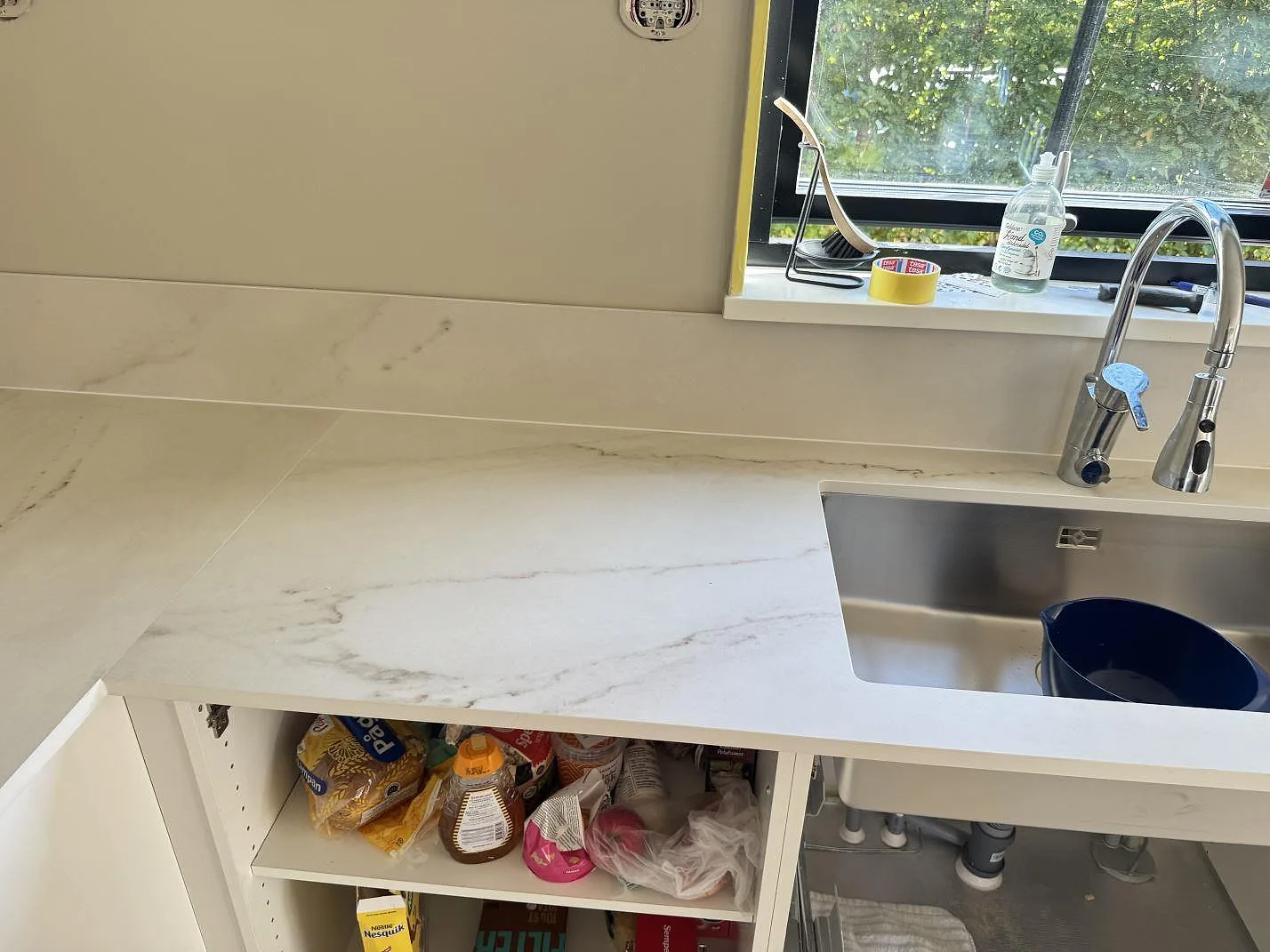 Lång köksbänk i matt Dekton Rem (Velvet), vit keramik med grå ådring, med rostfri diskho, blandare och stänkskydd i Båstad.