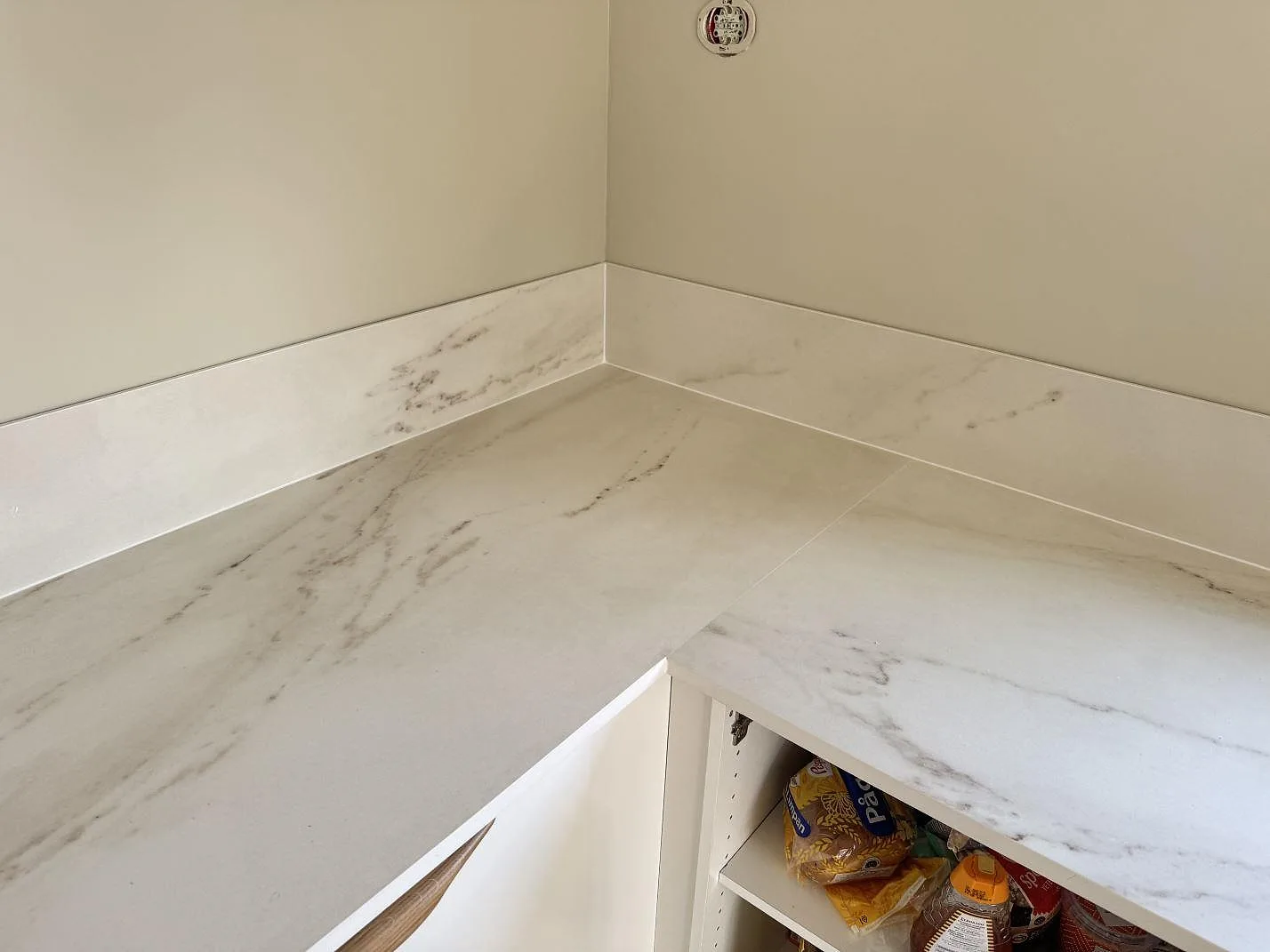 Hörn av köksbänkskiva i matt Dekton Rem (Velvet), ljus keramik, med matchande lågt stänkskydd och öppen köksstomme i Båstad.
