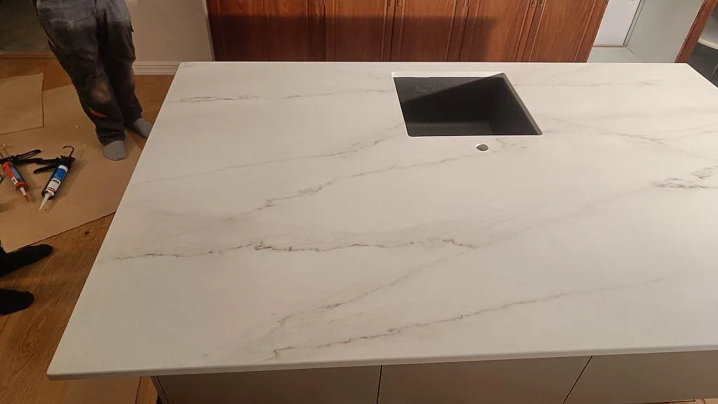 Köksö i vit Dekton Rem Velvet keramik i marmorlook med underlimmad mörk kompositdiskho och separat tapphål i ett kök i Eslöv.