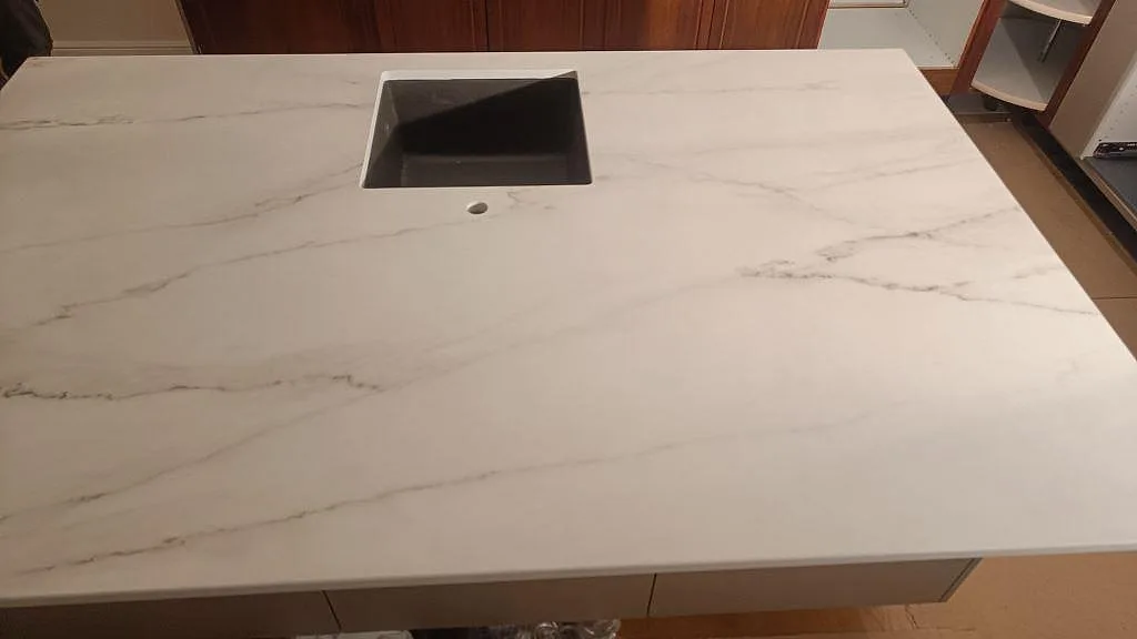 Matt vit Dekton Rem Velvet bänkskiva på köksö med fint grått ådringsmönster och underlimmad kompositdiskho i Eslöv.