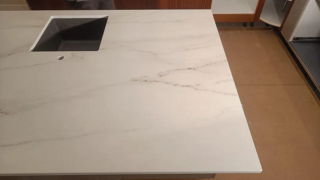 Närbild på köksö i Dekton Rem Velvet keramik med underlimmad mörk diskho och mjuk grå ådring i ett kök i Eslöv.