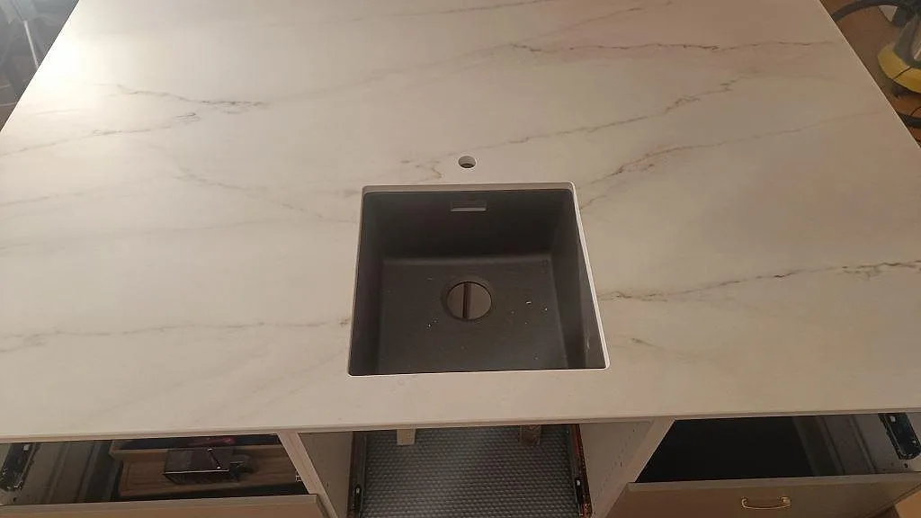 Underlimmad mörk kompositdiskho i vit Dekton Rem Velvet bänkskiva med tapphål i ett kök i Eslöv.