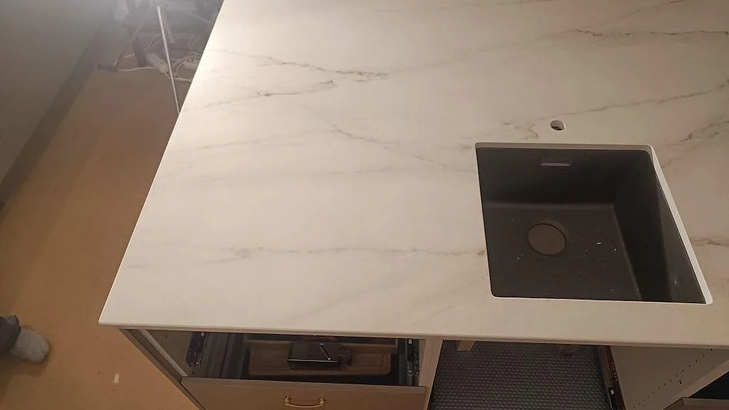 Vit Dekton Rem Velvet köksbänkskiva i marmorlook med underlimmad kompositdiskho över öppna stommar under montering i Eslöv.