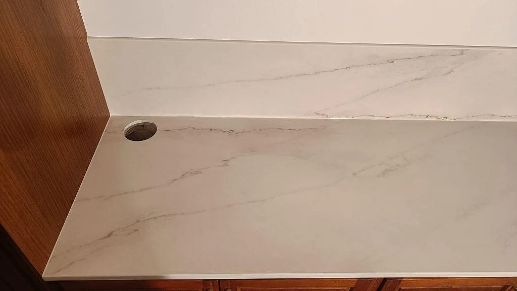 Köksbänkskiva i vit Dekton Rem Velvet keramik med uppvikt stänkskydd och blandarhål mot träinredning i ett kök i Eslöv.