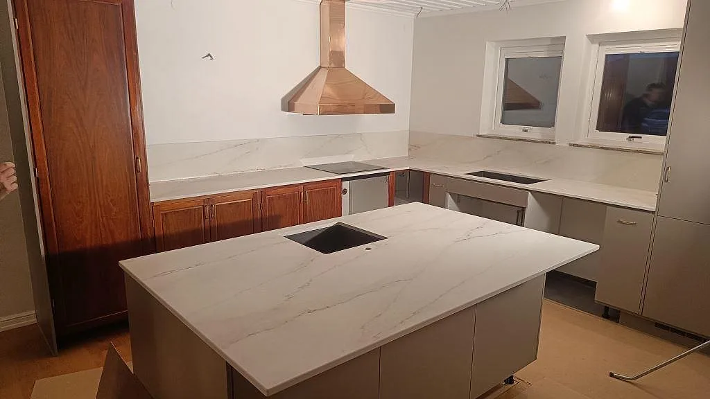 Köksbänkskiva och köksö i vit Dekton Rem Velvet, matt keramik med grå ådring, med kopparfläkt och plats för induktionshäll i ett kök i Eslöv.