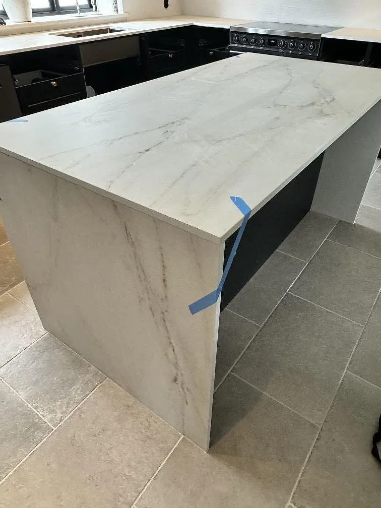 Köksö i matt Dekton Rem (Velvet) med vit marmorerad yta och vattenfallsida i ett kök i Glumslöv.