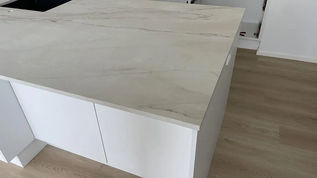 Hörnvy av köksö i matt Dekton Rem (Velvet) med ljus bänkskiva, grå ådring och vita stommar i Hvidovre.