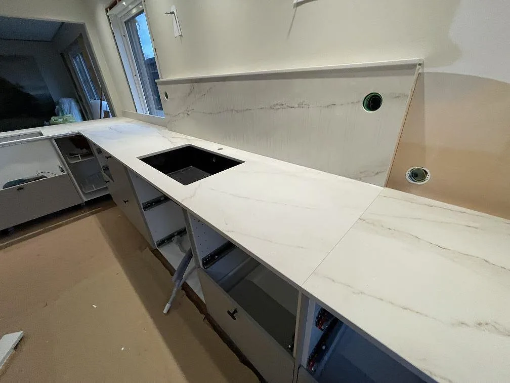 Detalj av ljus Dekton Rem (Velvet) i matt finish med svart diskho och högt stänkskydd med eluttag i kök i Kristinehamn.