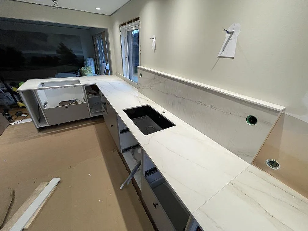 Vinkelvy över köksbänkskiva i Dekton Rem (Velvet), matt keramik, med stänkskydd, svart diskho och öppna stommar i Kristinehamn.