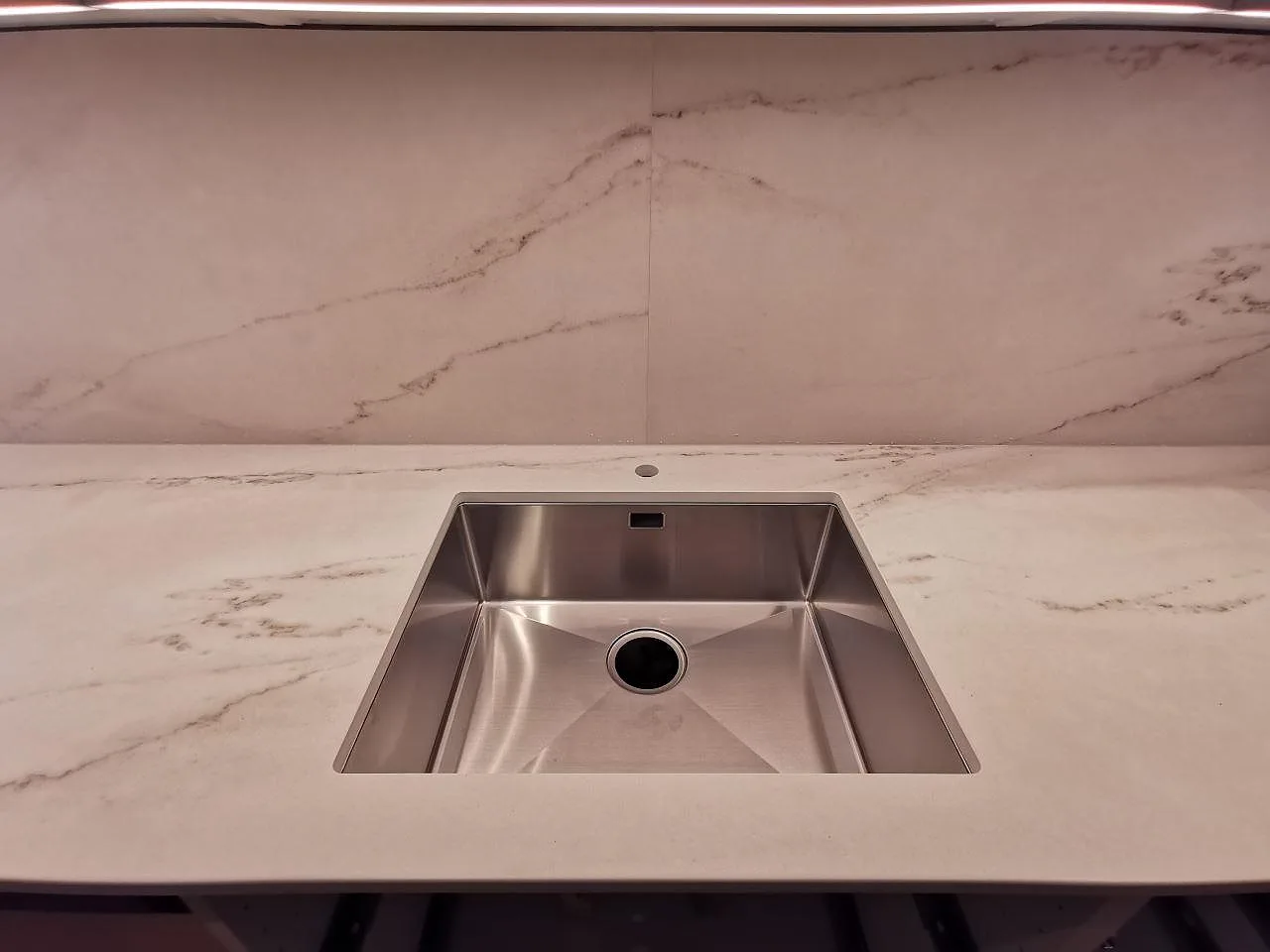 Underlimmad rostfri diskho infälld i en matt köksbänkskiva i Dekton Rem Velvet keramik med uppvikt stänkskydd i Limhamn.