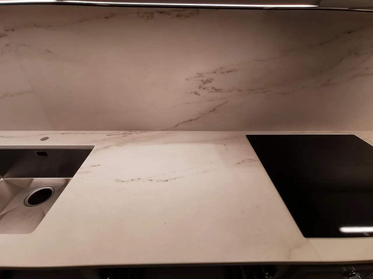 Köksbänkskiva i Dekton Rem Velvet, matt keramik med mjuk grå ådring, med underlimmad rostfri diskho och övermonterad induktionshäll samt uppvikt stänkskydd i ett kök i Limhamn.